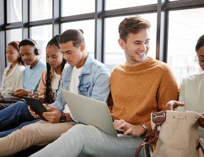 diverse Gruppe von Studenten auf dem Boden mit Laptops vor einem Fenster sitzend